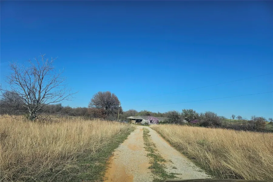 Gravel driveway leading to a residence with a visible garage and surrounding acreage