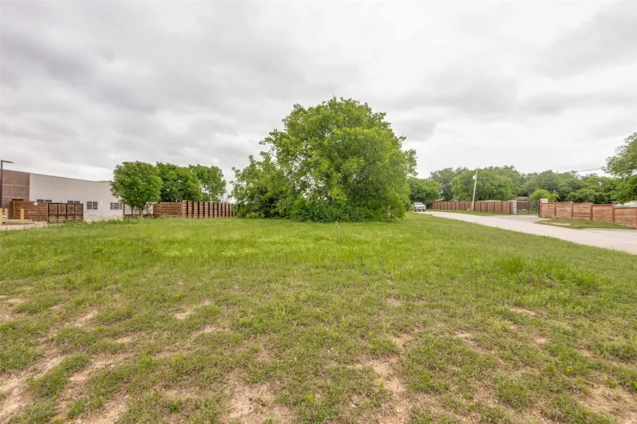 Expansive grassy lot with mature trees, established roadway, and perimeter fencing
