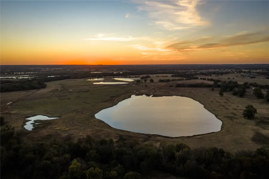 Aerial view of scenic pond and rolling ranch landscape at sunset.