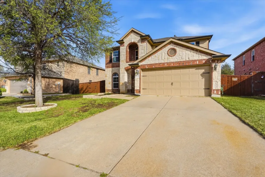 French country inspired facade with a gate, stone siding, an attached garage, driveway, and brick siding