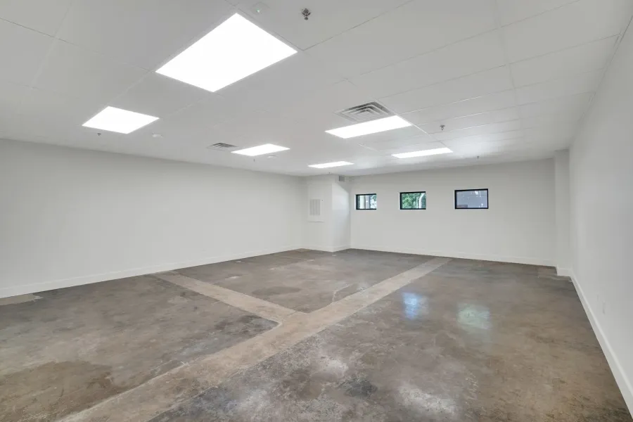 Spacious room featuring concrete flooring, white walls, multiple rectangular windows, a white drop ceiling, and recessed lighting