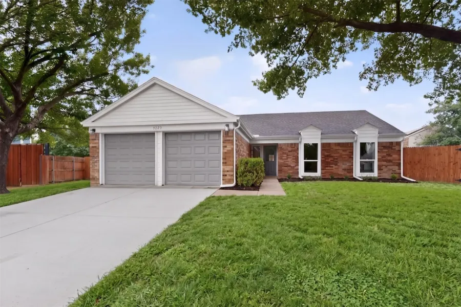 Brick exterior featuring a two-car garage with gray doors, a dark gray front door, and two prominent bay windows