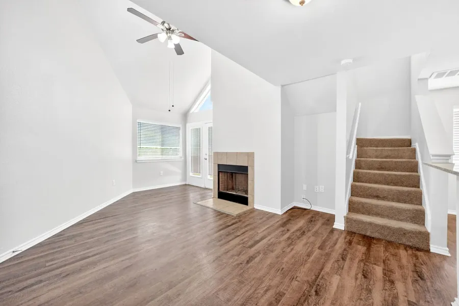 Spacious living area featuring vaulted ceilings, wood-finish flooring, a fireplace with a tiled surround, a ceiling fan, and access to an outdoor area