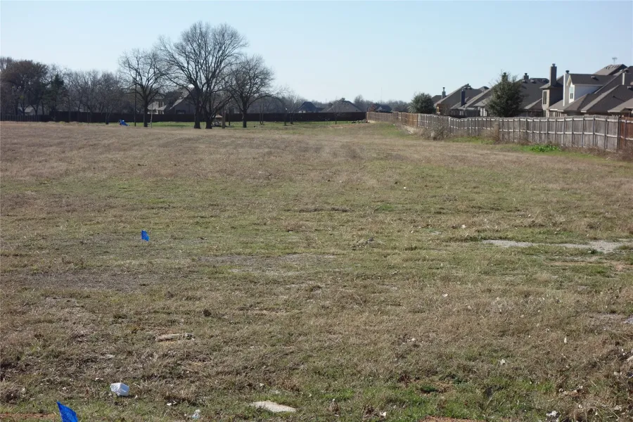 Expansive open lot with distant residential structures and mature deciduous trees