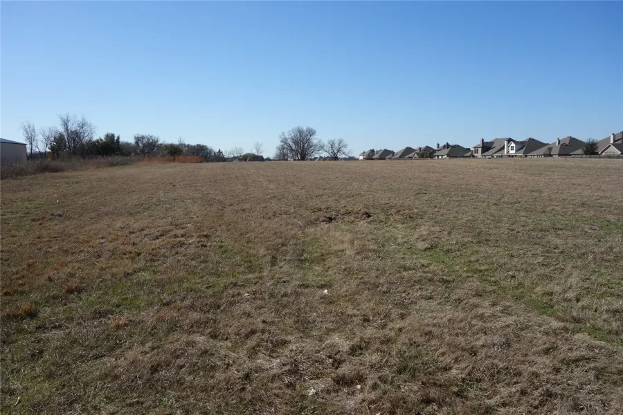 Expansive undeveloped land parcel featuring a clear sky and distant residential structures