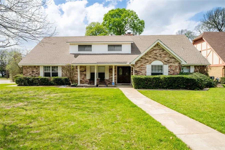 View of front facade with covered porch, a front yard, roof with shingles, and brick siding