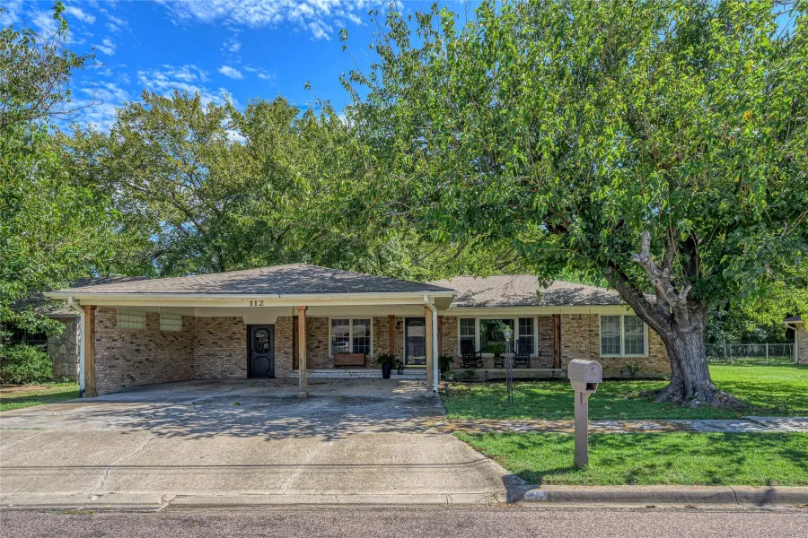 Ranch-style home with a front yard, driveway, a carport, a porch, and brick siding