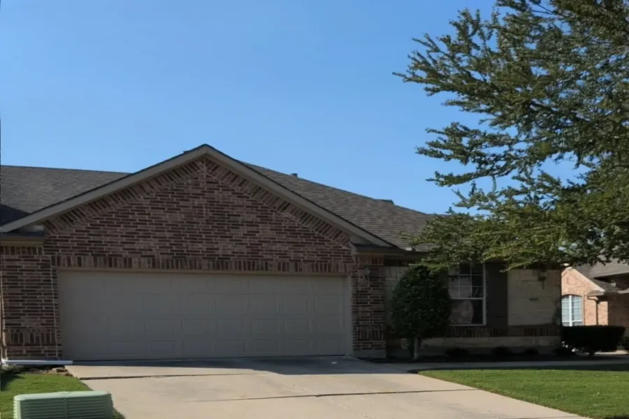 Ranch-style house featuring an attached garage, brick siding, driveway, and a shingled roof