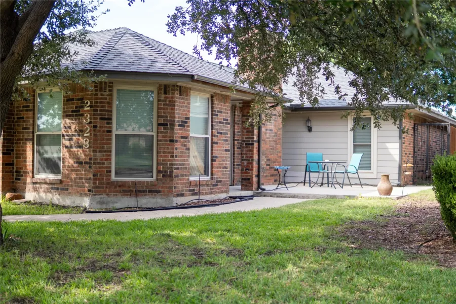 Rear view of house featuring brick siding, a lawn, a shingled roof, and a patio area