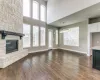 Unfurnished living room with a stone fireplace, healthy amount of natural light, dark wood-type flooring, and a towering ceiling