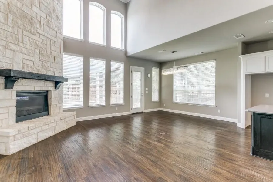 Unfurnished living room with a stone fireplace, healthy amount of natural light, dark wood-type flooring, and a towering ceiling