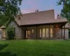Back of house at dusk with a yard, brick siding, a shingled roof, and a patio area