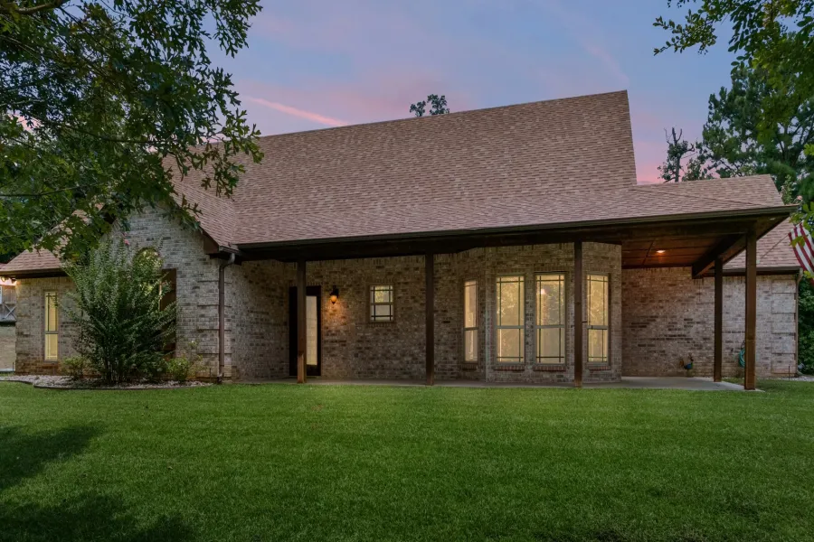 Back of house at dusk with a yard, brick siding, a shingled roof, and a patio area