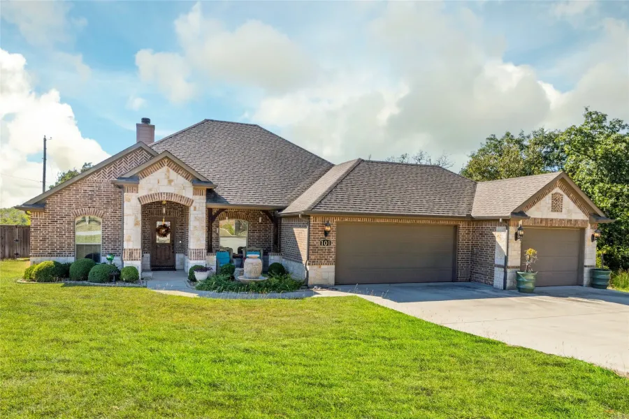 French country inspired facade featuring brick siding, a front lawn, an attached garage, and roof with shingles