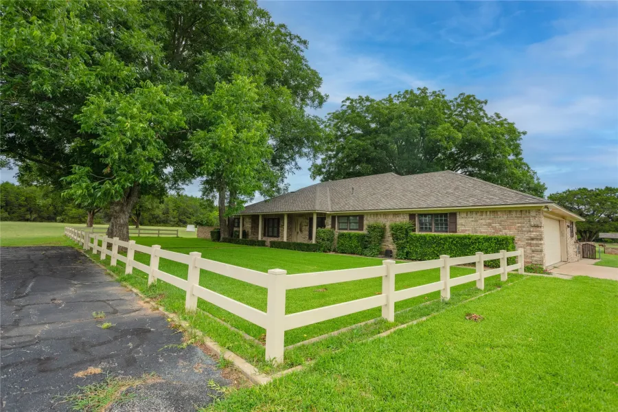 Ranch-style home with a fenced front yard, an attached garage, driveway, roof with shingles, and brick siding