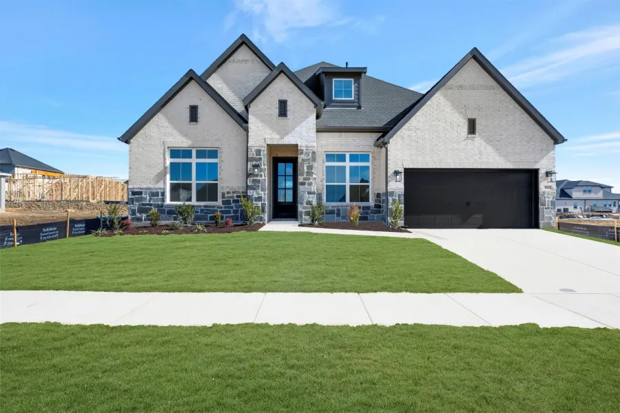 View of front facade with a front lawn, stone siding, brick siding, concrete driveway, and an attached garage