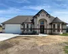 French country inspired facade featuring stone siding, roof with shingles, concrete driveway, and a garage