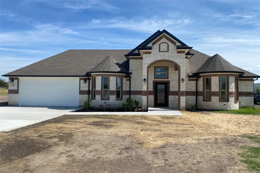 French country inspired facade featuring stone siding, roof with shingles, concrete driveway, and a garage