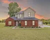 Traditional home with a shingled roof, a yard, brick siding, and a garage
