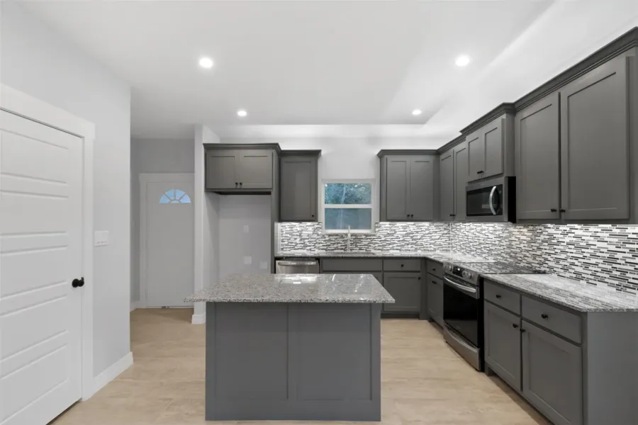 Kitchen with light stone counters, gray cabinets, a center island, appliances with stainless steel finishes, and backsplash