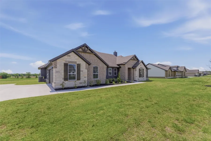 Exterior featuring a stone and brick facade, dark trim, an attached garage, a concrete driveway, and a manicured lawn