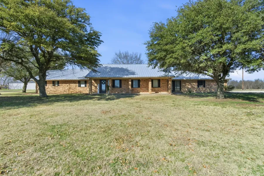 Ranch-style home with a front yard, a metal roof, brick siding, and covered porch