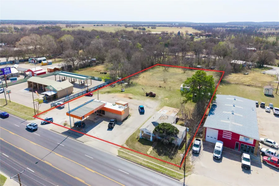 Expansive commercial property featuring significant road frontage, a paved parking area, multiple structures, and undeveloped land