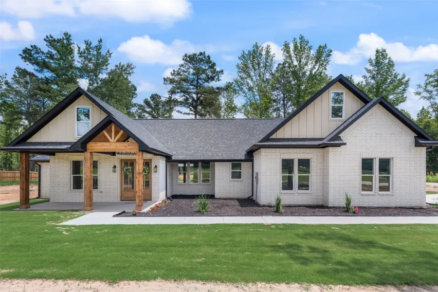 Modern farmhouse exterior featuring white brick, dark-trimmed gables, a covered front porch with substantial wood columns, and a double wood-paneled entry door