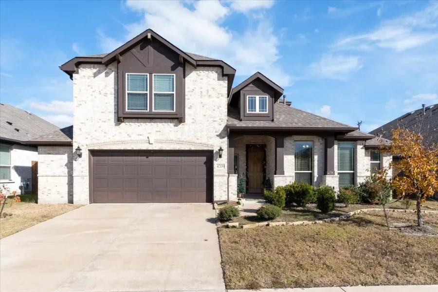 Two-story home featuring a light brick exterior with dark trim accents, a two-car garage, and a covered front entry